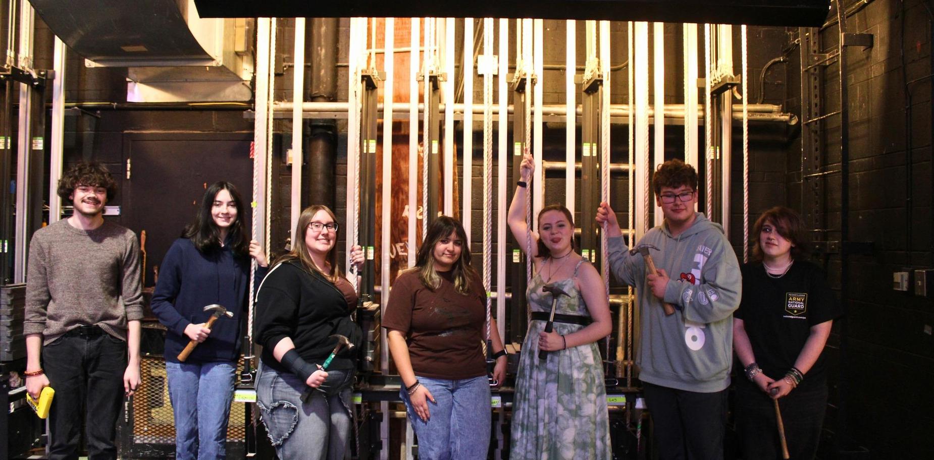Group of seven people holding tools on a theater stage.