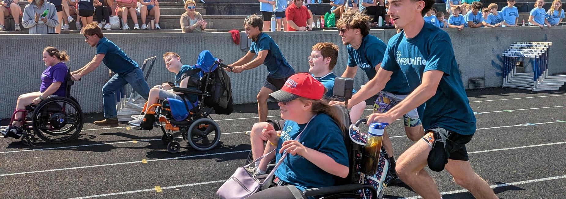 three students participating in a wheelchair races on the track