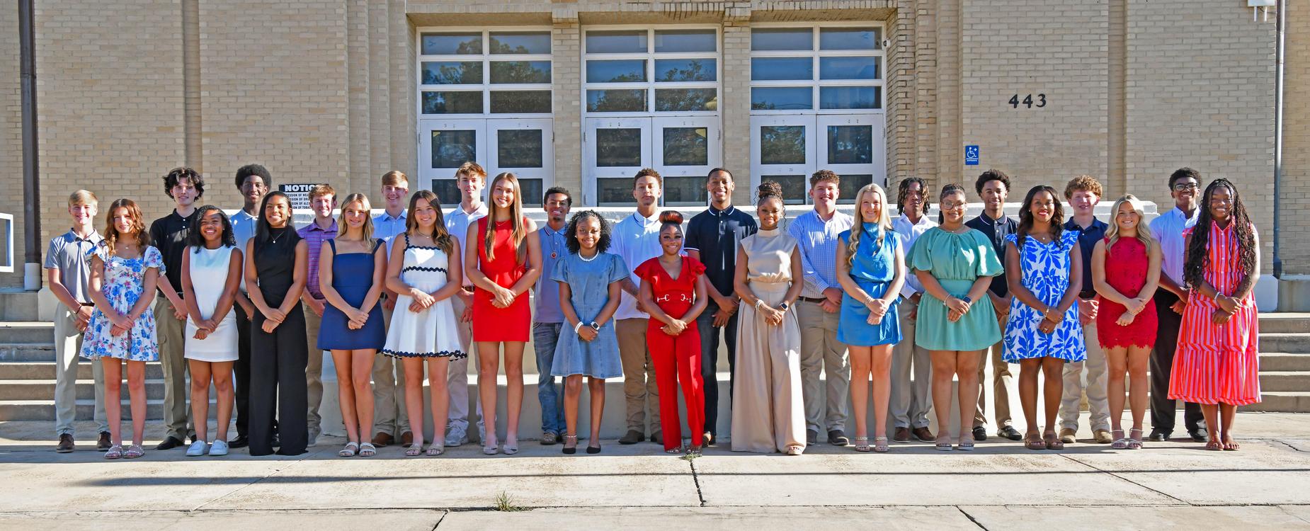 A diverse group of people posing together in front of a school building.