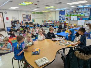 Students reading books at tables in a colorful classroom with educational materials.