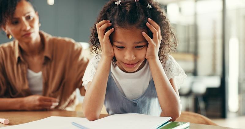 Student struggles with homework while a concerned parent looks on