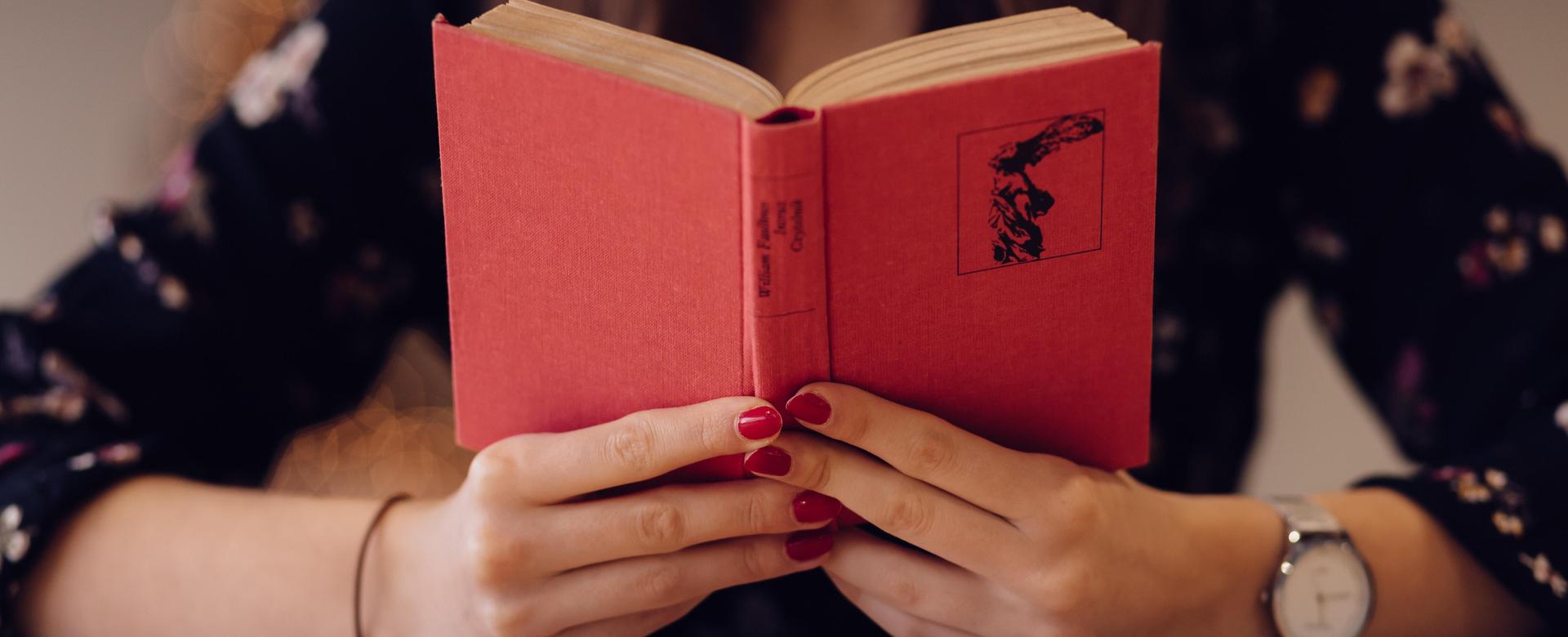 A person holding a red book with a floral background.
