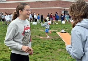 A girl smiling while talking to an adult with a clipboard in a grassy area.