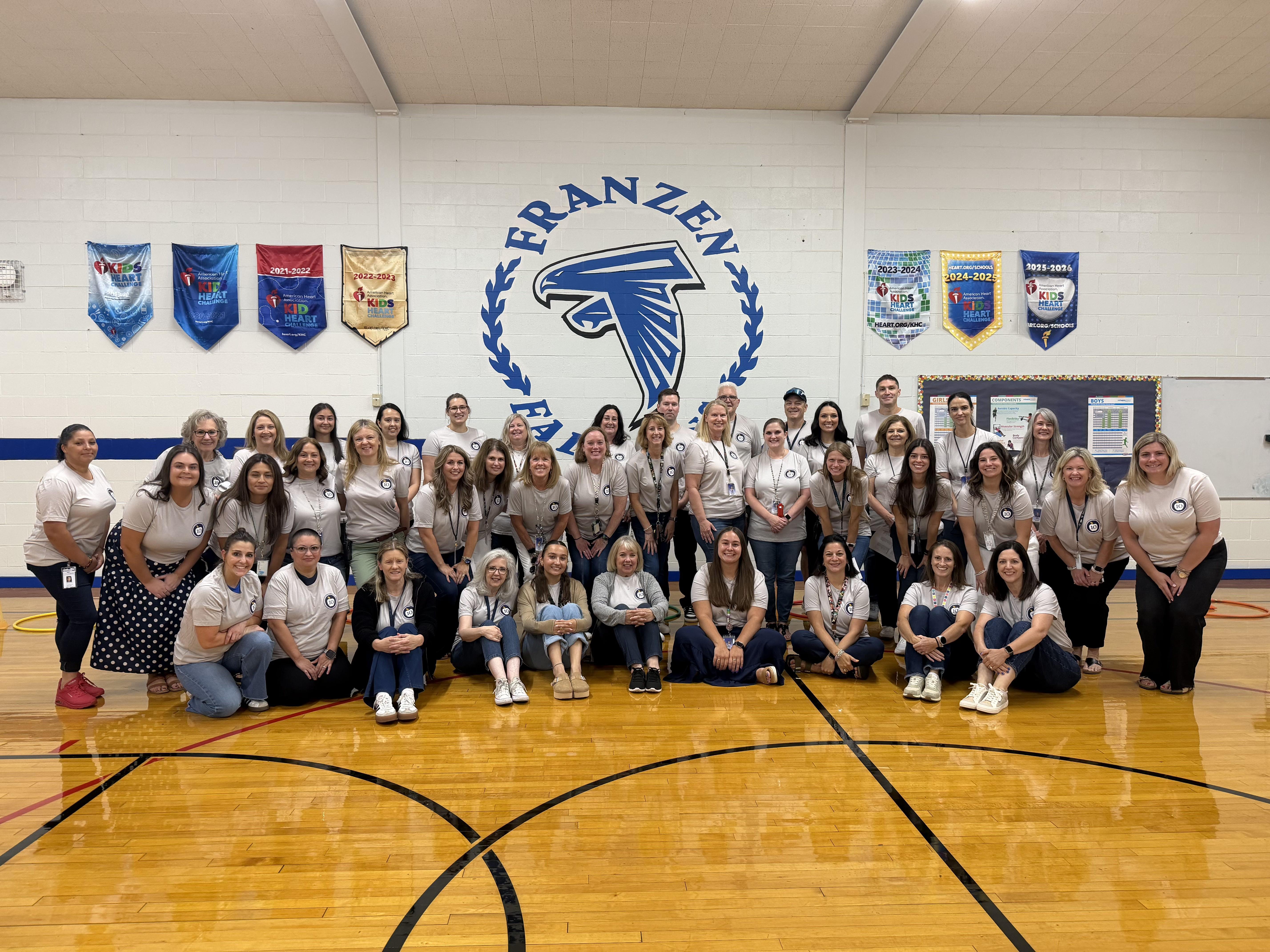 franzen intermediate school staff standing inside the gym with a falcons logo in the background and matching school shirts