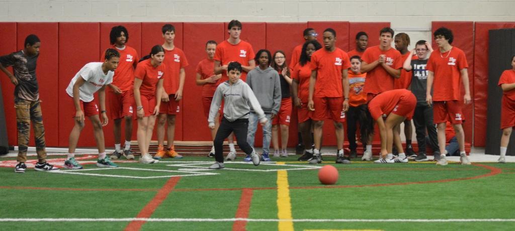 student prepares to kick a ball with several high school behind cheering