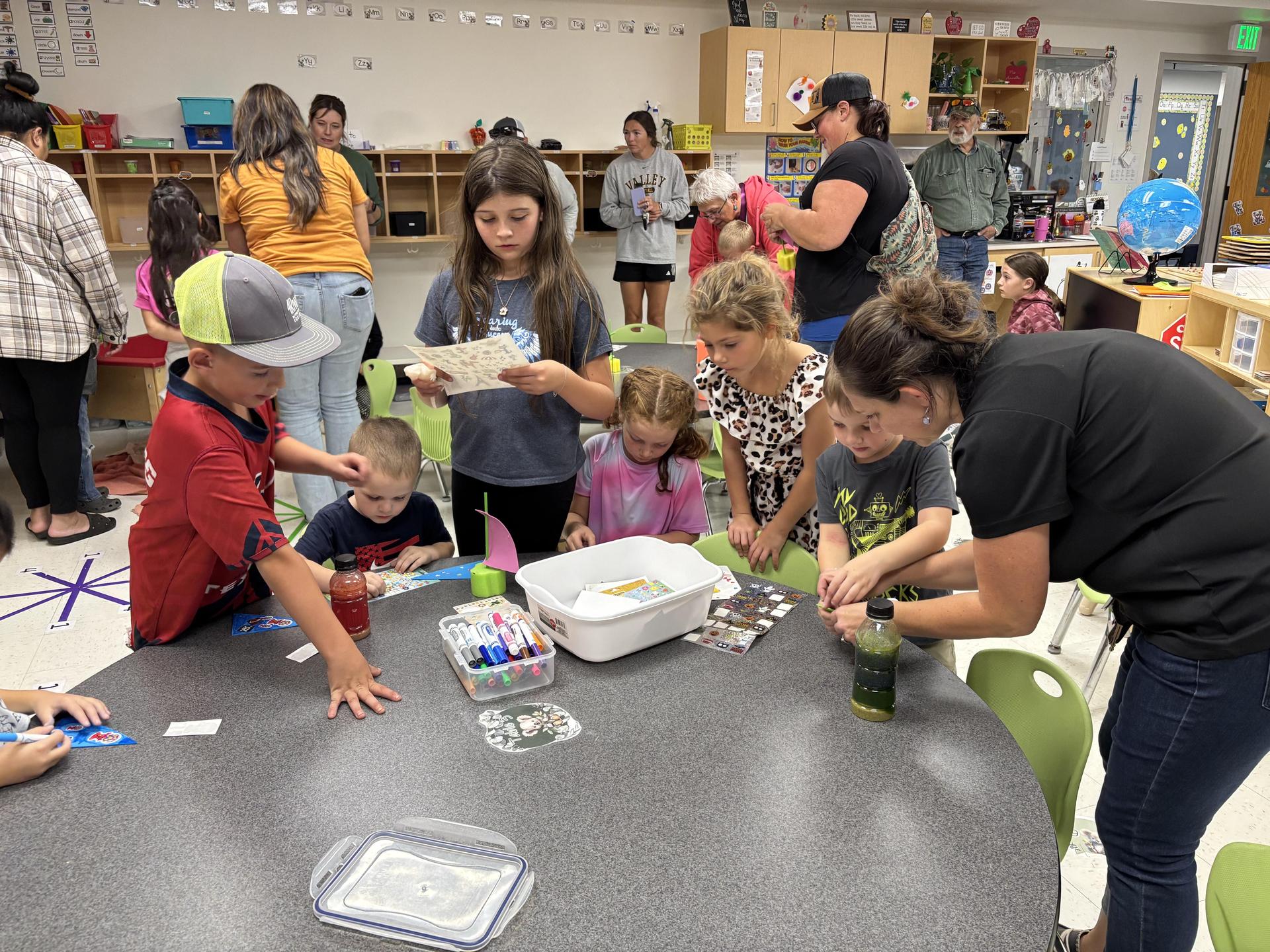 Kids working on crafts and activities at a busy classroom table with adults supervising.