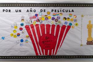 A bulletin board at Arco Iris Spanish Immersion School says “por un ano de pelicula” and has a large image of a striped popcorn bucket and colorful popcorn pieces.