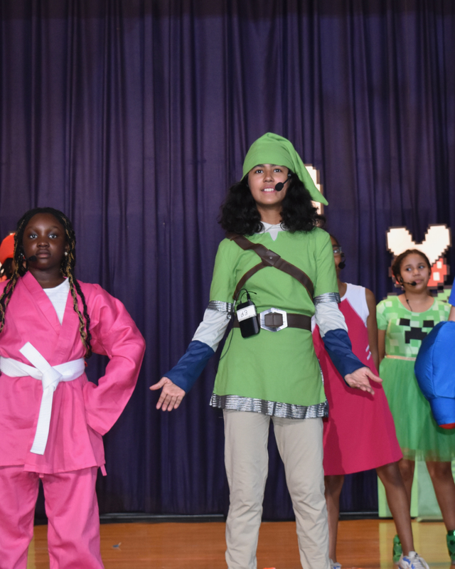 Student singing in green costume with hat
