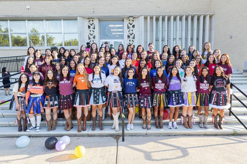 Large group of girls in colorful shirts posing on steps with balloons.