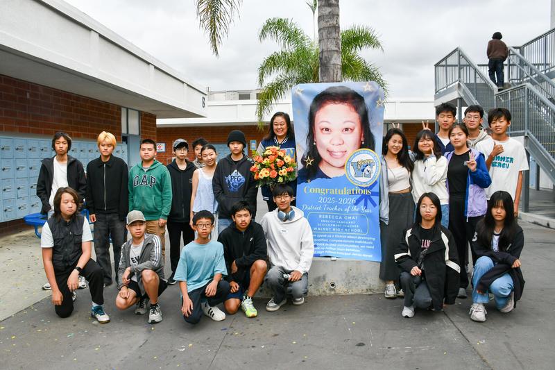 Rebecca Chai and her students pose beside a banner celebrating her District Teacher of the Year recognition.