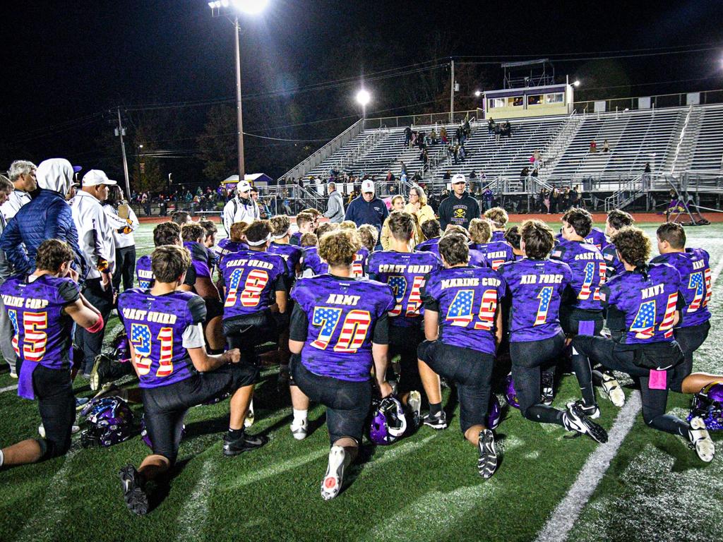 Football players kneeling and wearing jerseys to honor the military.