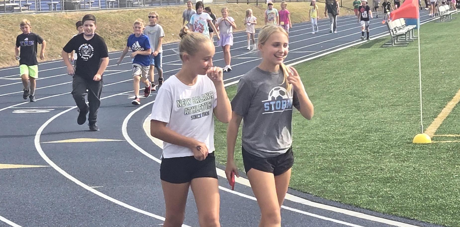 Two girls walking side by side on a track, chatting and smiling.