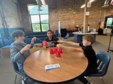 Three kids collaborating to stack red cups on a table.