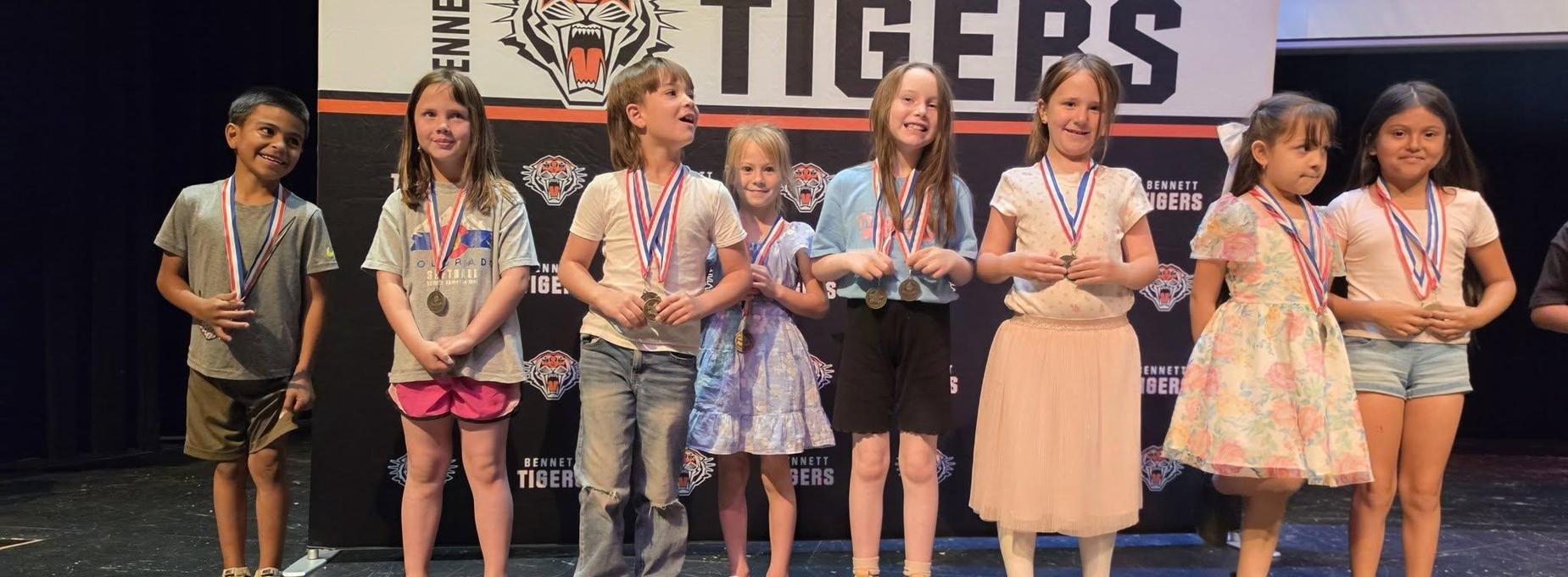 Children standing in a line wearing medals at an award ceremony.
