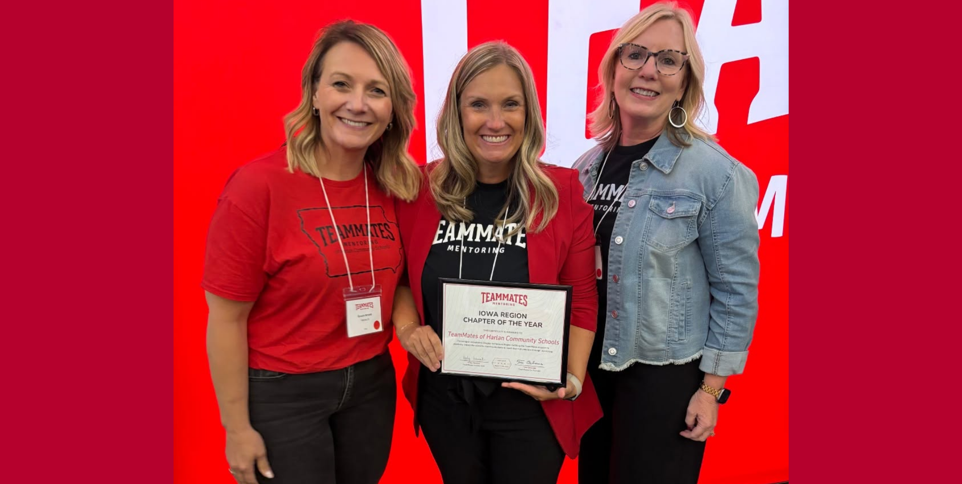 Three women celebrate holding an award in front of a red background.