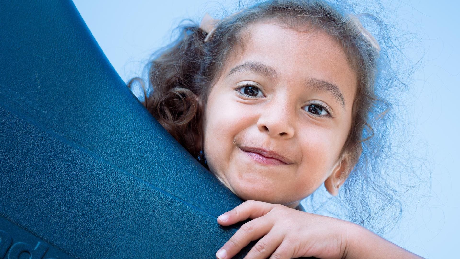 Girl with curly hair playfully peeking over a black object.