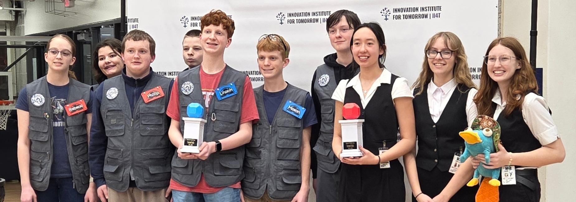 Group of students holding trophies, posing together at an event. Vex Robotics competition.