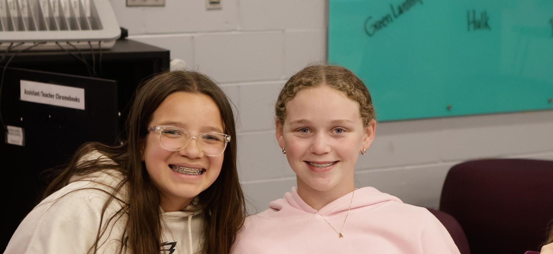 Two smiling girls sitting together in a classroom.