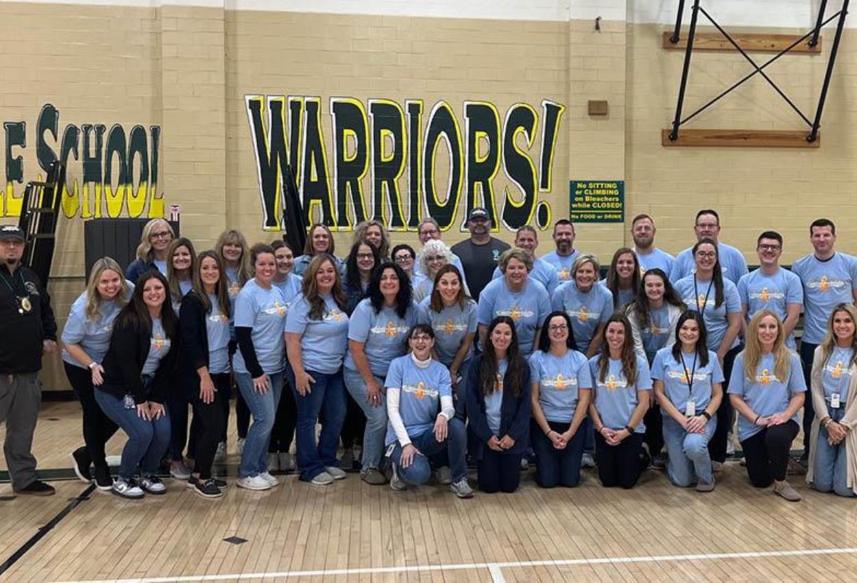 Photo has all the Penn Middle School staff gathered in the gym with matching shirts