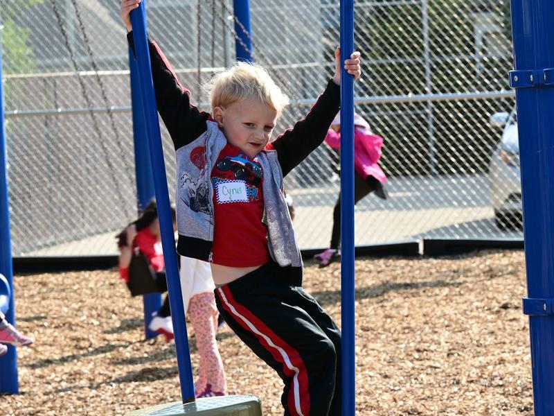 A boy climbs a swing set on a playground, wearing a red shirt.