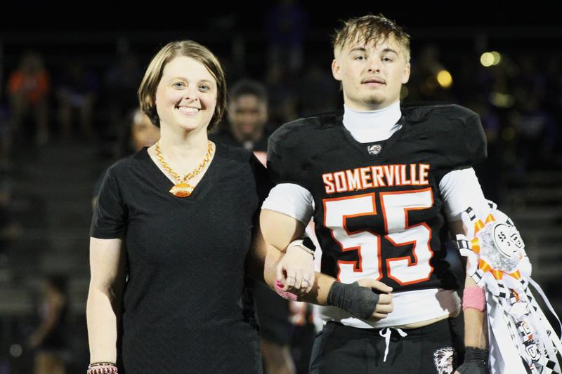 A young man in a football uniform walks with a woman on the field.