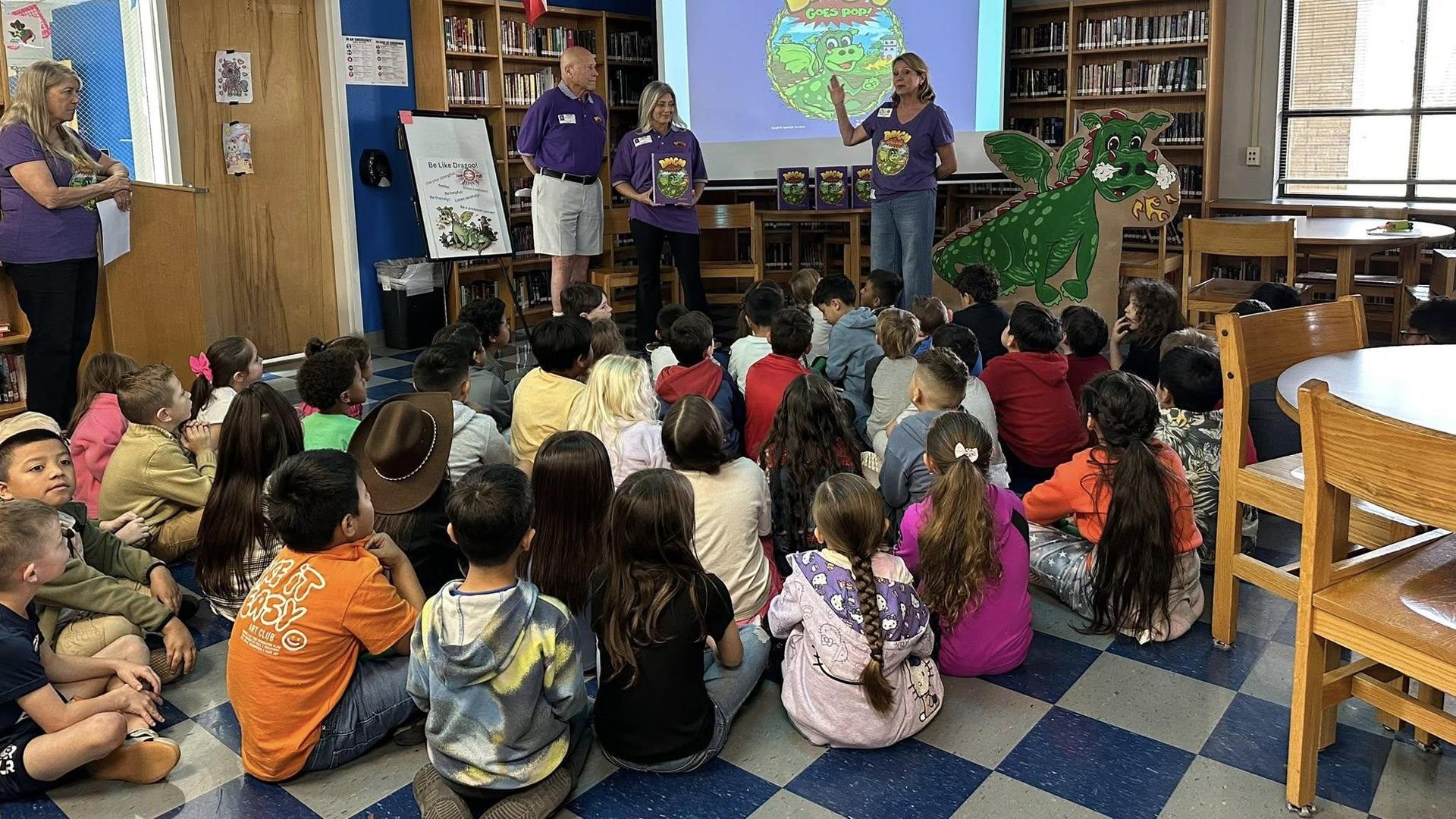 Children seated in a library watching a presentation by adults.