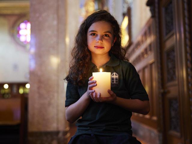 Girl with curly hair holding a lit candle in a dimly lit church interior.