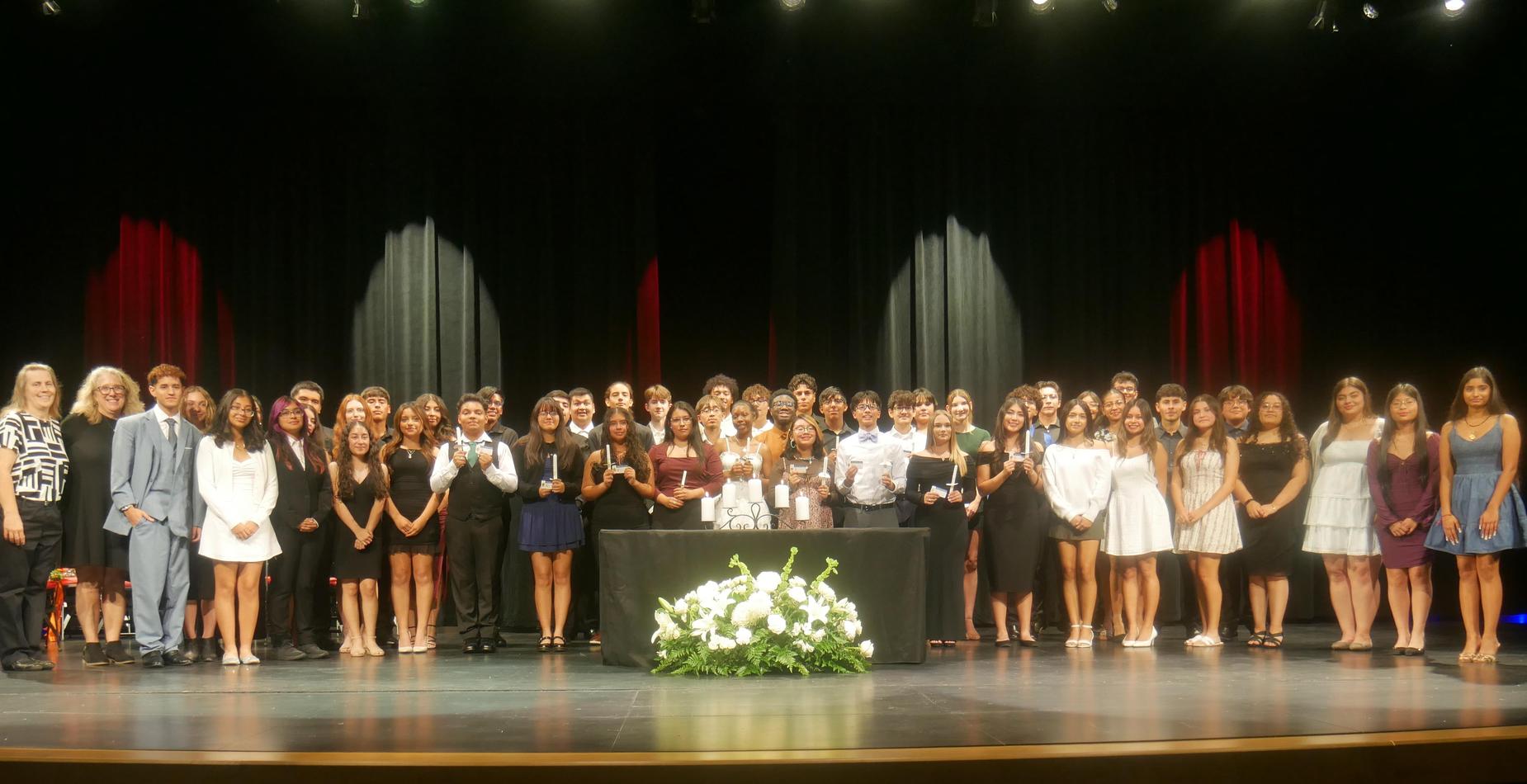 Group stands and smiles while some hold candles