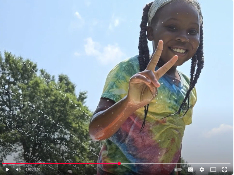 Image shows a young girl wearing a Mandela tie dye shirtholding up a peace sign