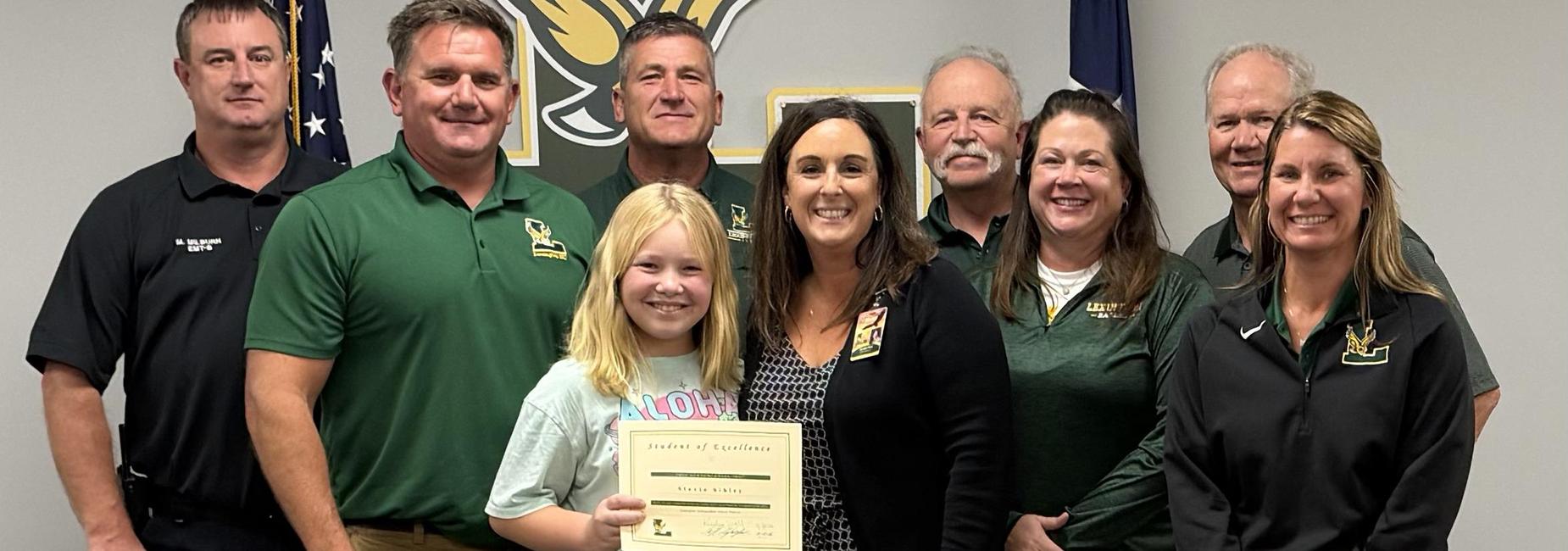 Group of people posing with a girl holding a certificate of excellence.