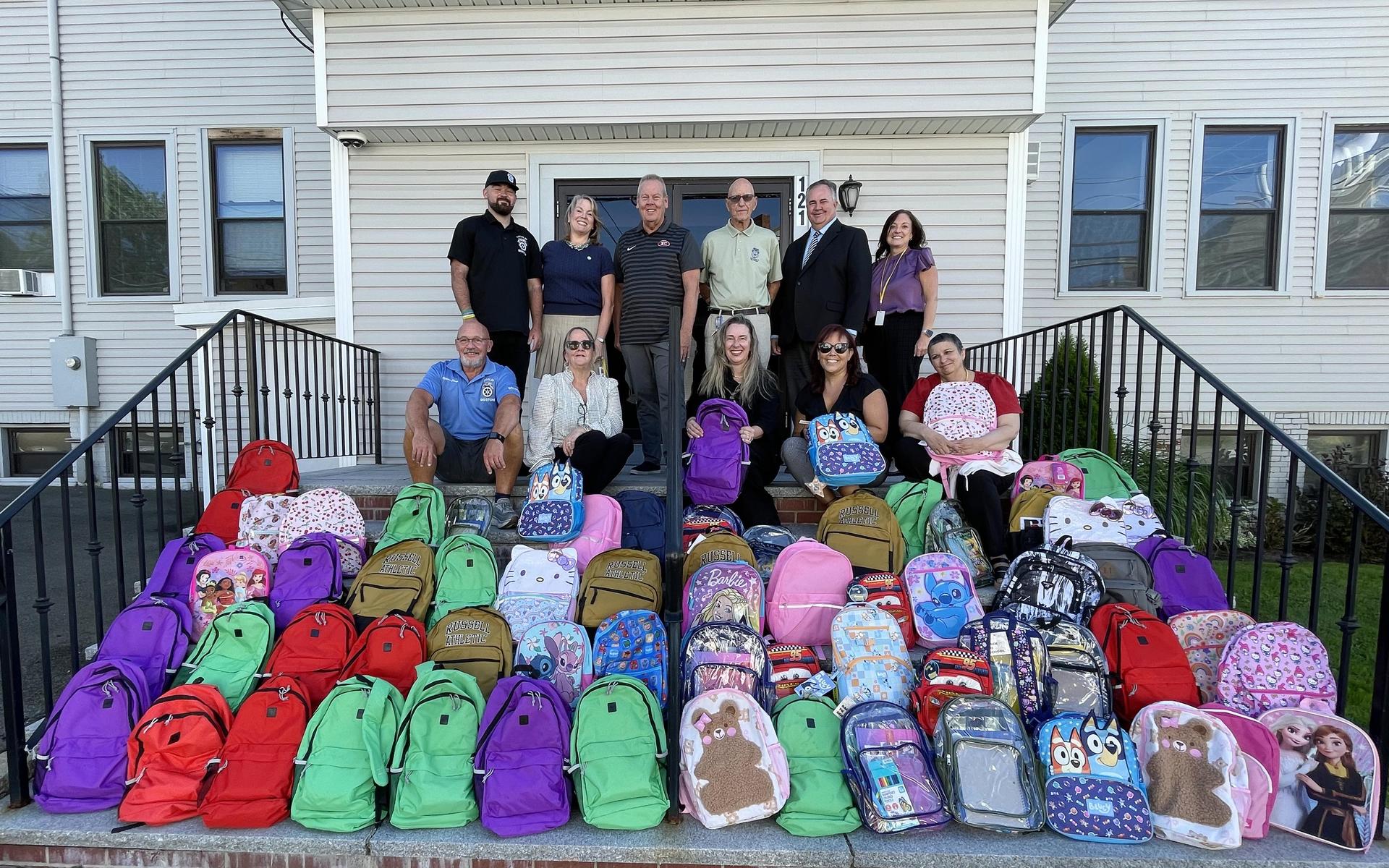 Group of people posing on stairs with colorful backpacks in front.