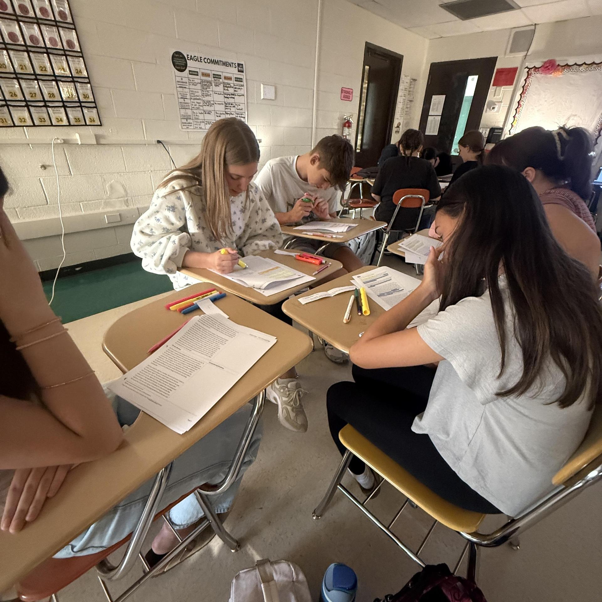 Students engaged in study at desks, focusing on their work with notebooks and pens.
