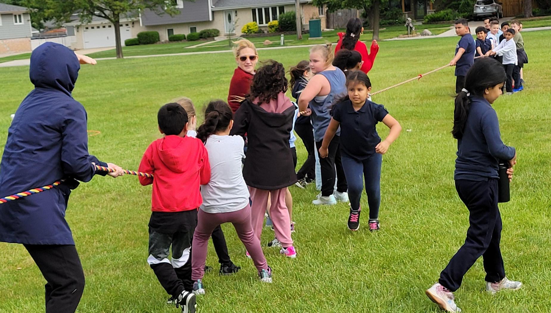 Children participating in a tug-of-war in a grassy area.