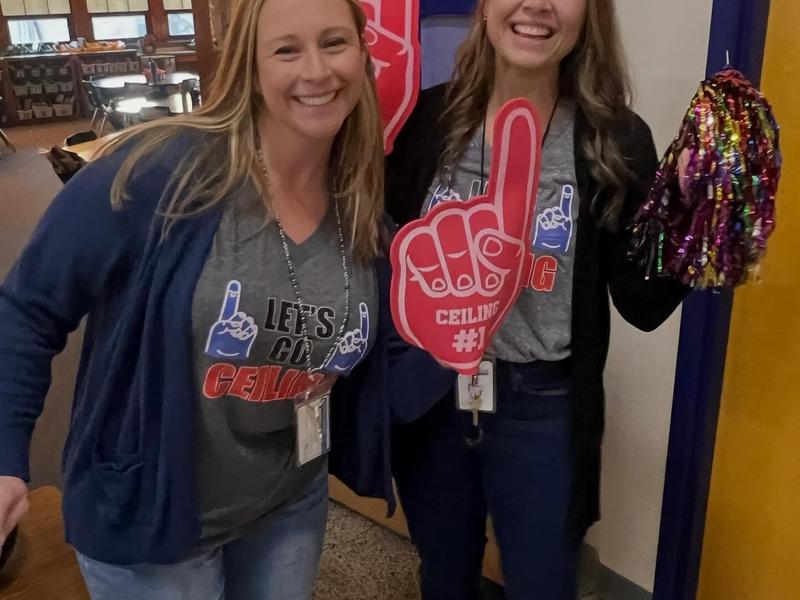 Two women smiling and holding cheering props in a school environment.
