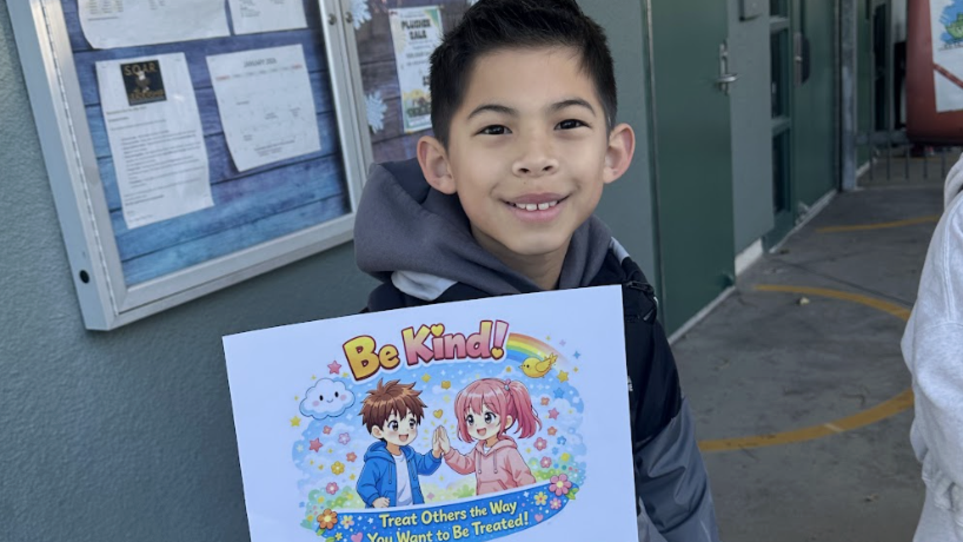 Child holding a sign that reads 'Be Kind!' with colorful cartoon characters.