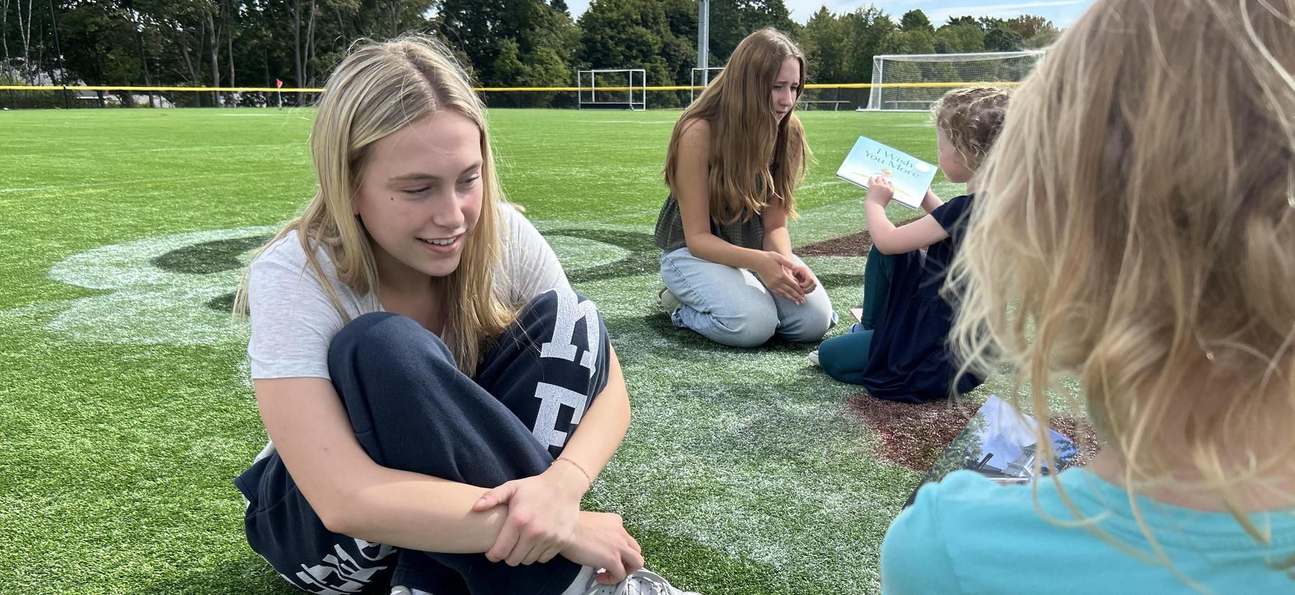 Group of children and teens sitting on grass, engaged in a conversation.