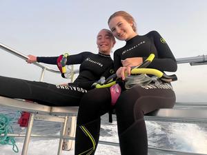 Two Students in Wetsuits on a boat smiling.