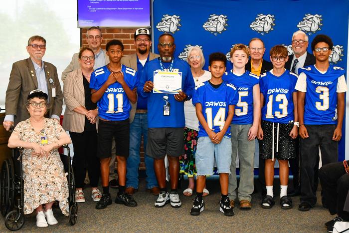 A group of football players, a coach, and board members smiling and holding an award