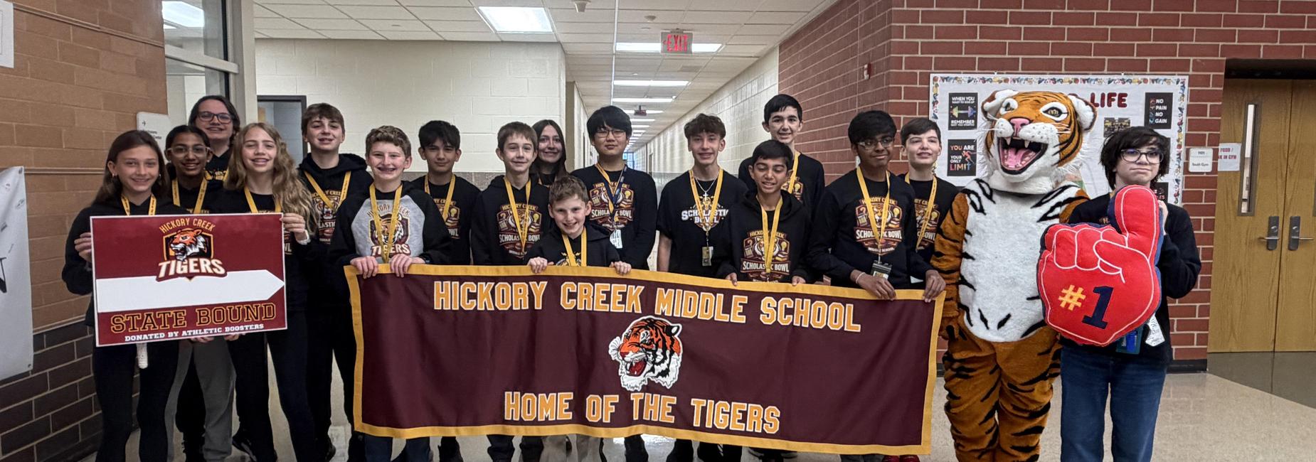 Group of students and a mascot posing with a banner at Hickory Creek Middle School.