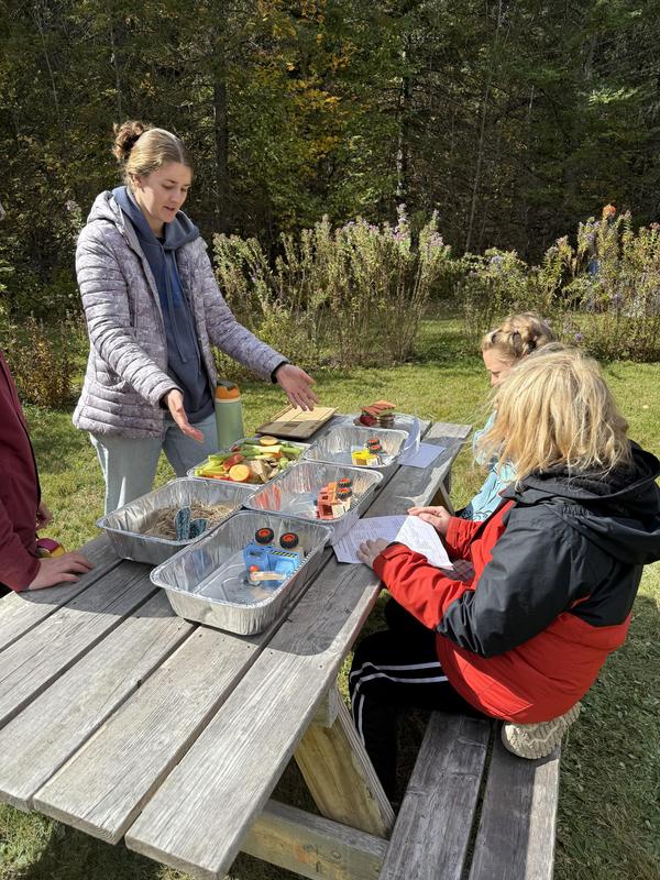Two girls discussing items on a picnic table filled with snacks.