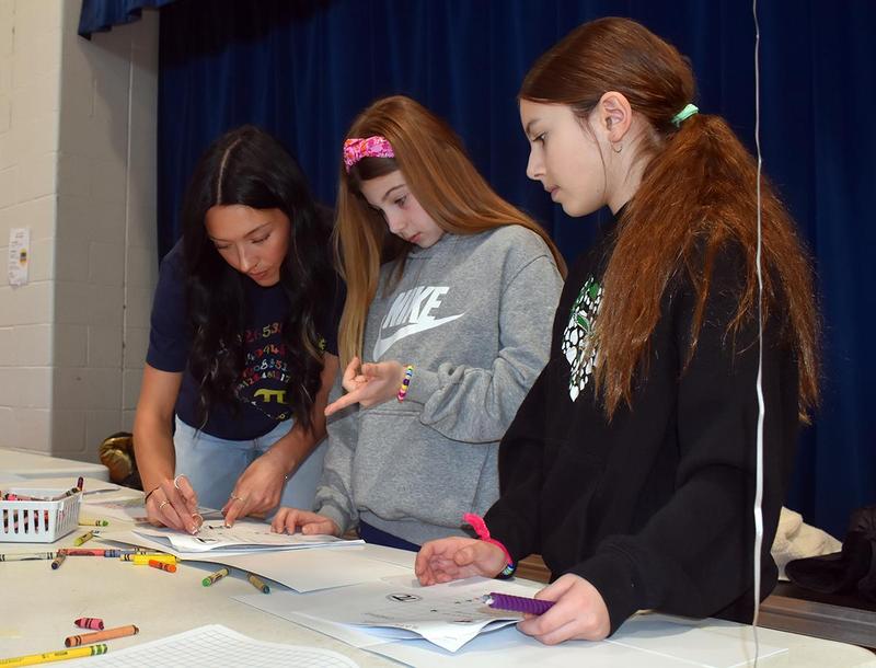 a college student helping two girls complete a writing activity
