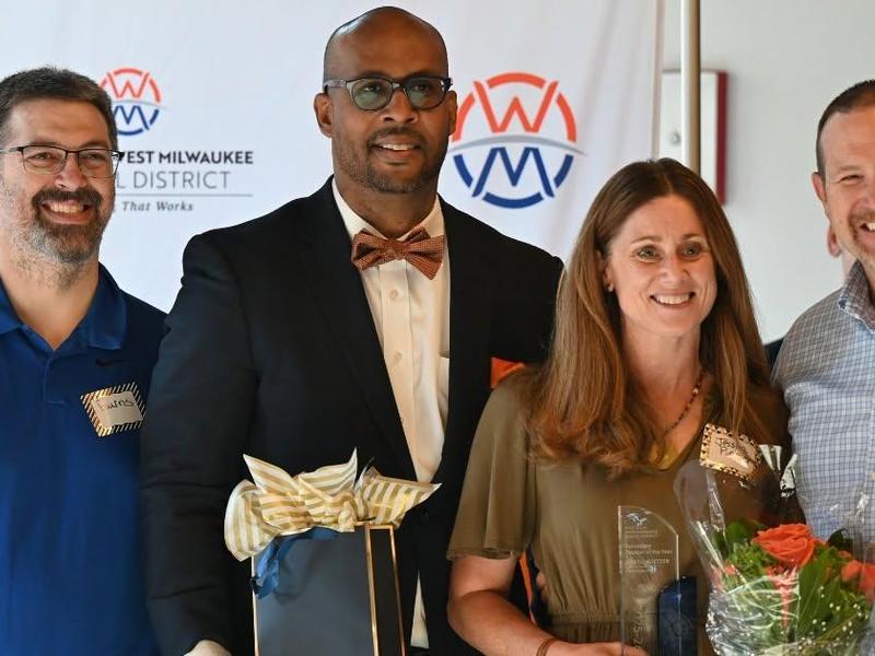 Group of four people celebrating an award, holding gifts and flowers.