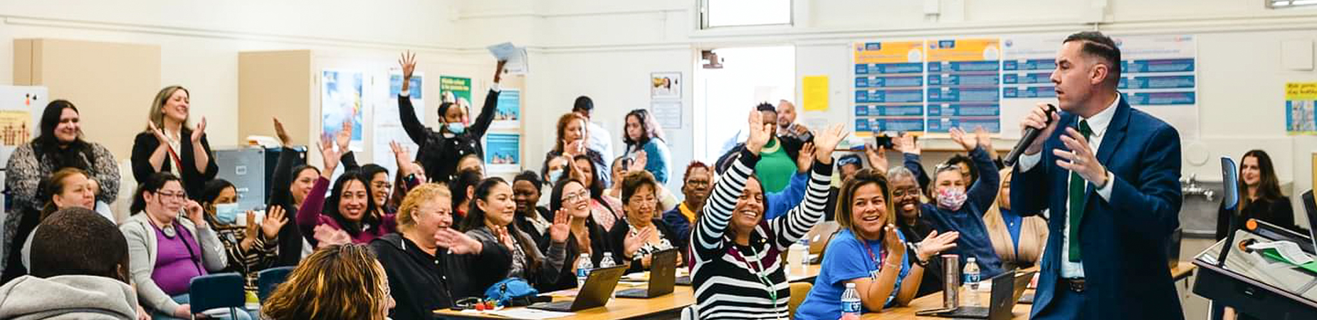 A man speaks in a classroom of parents who are clapping