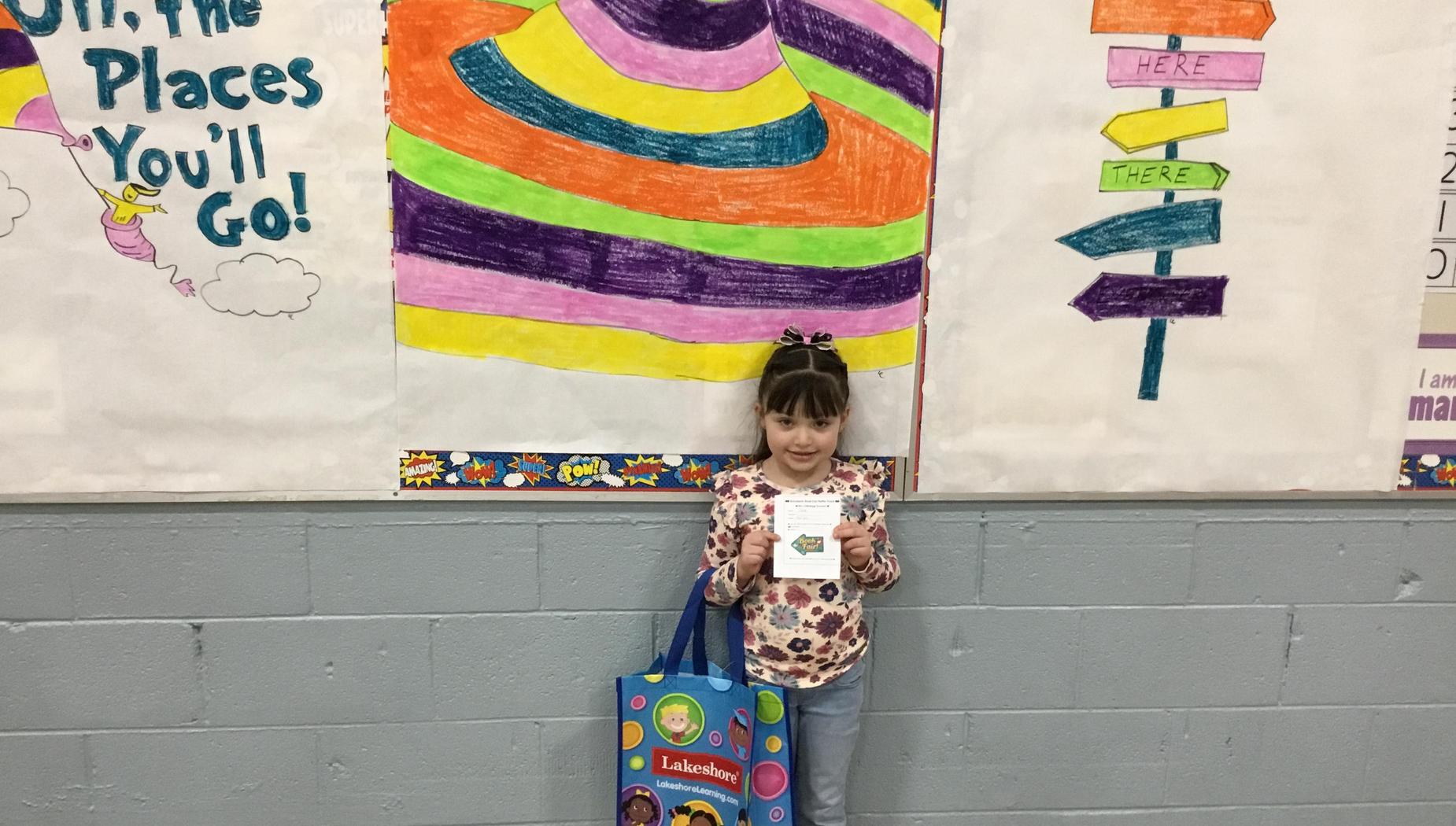 Child with a bag holding a certificate in front of a colorful mural and signs.