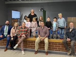 adults sitting on ledge of stage smiling, small children standing on stage with teacher smiling