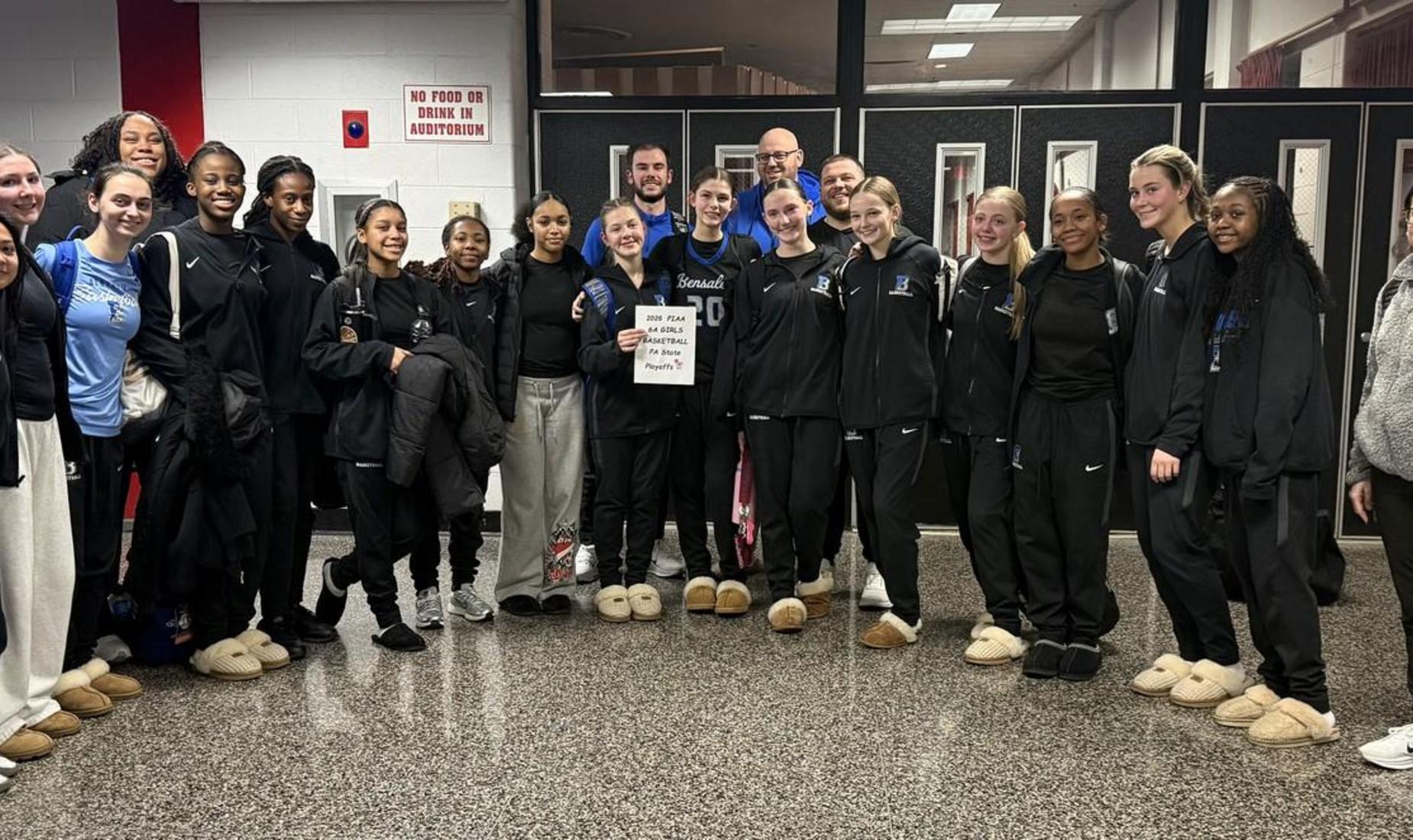 Image of the BHS Basketball Team posing together in matching tracksuits, smiling and holding a sign.