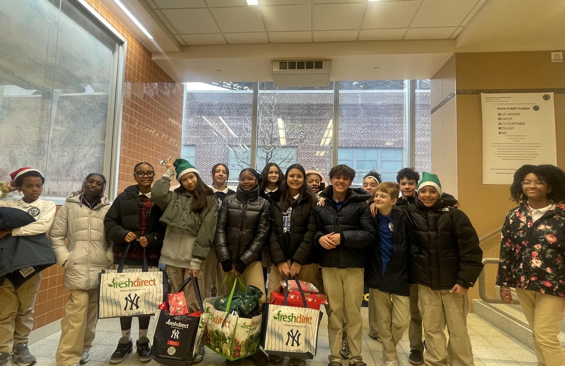 A group of children and adults posing together in a hallway, smiling and holding shopping bags.