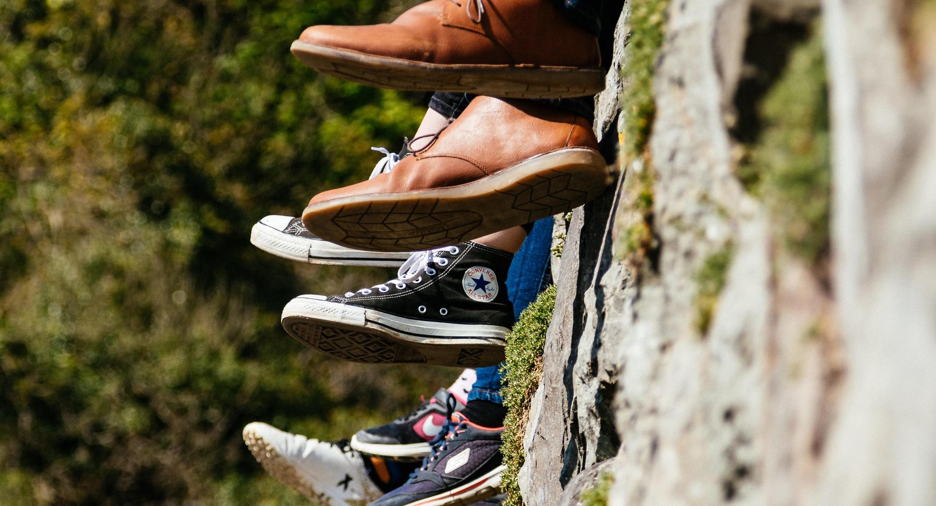 A row of children sitting on a wall only visible by their shoes in a row
