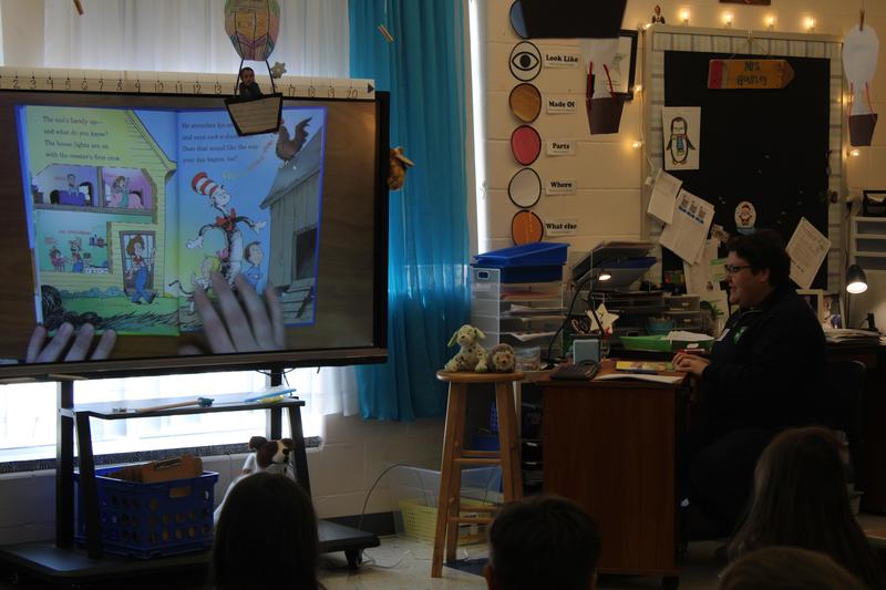 Dr. Suess book on screen with reader seated beside book