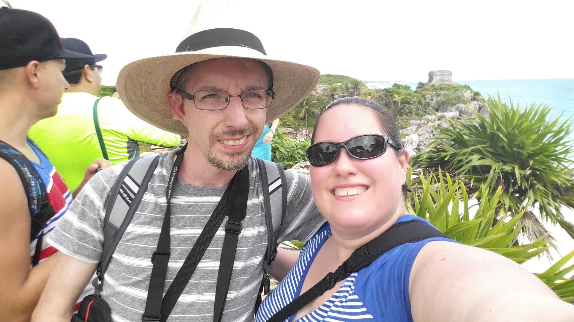 A selfie of Tracy and Chris smiling at the camera standing near the coast in the ruins of Tulum. 
